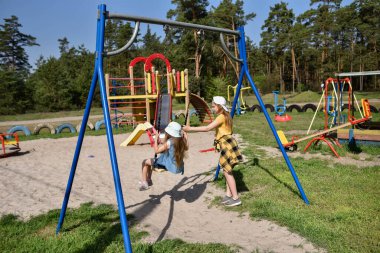 İki sarışın liseli kız salıncakta sallanıyor bir çocuk parkında çam ormanının yakınında