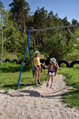 İki sarışın liseli kız salıncakta sallanıyor bir çocuk parkında çam ormanının yakınında