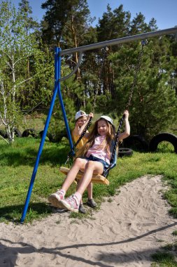 İki sarışın liseli kız salıncakta sallanıyor bir çocuk parkında çam ormanının yakınında