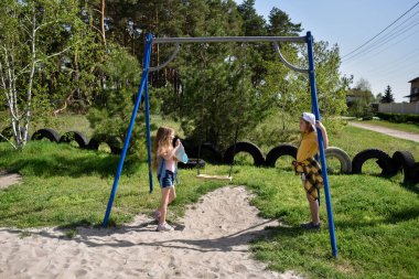 İki sarışın liseli kız salıncakta sallanıyor bir çocuk parkında çam ormanının yakınında