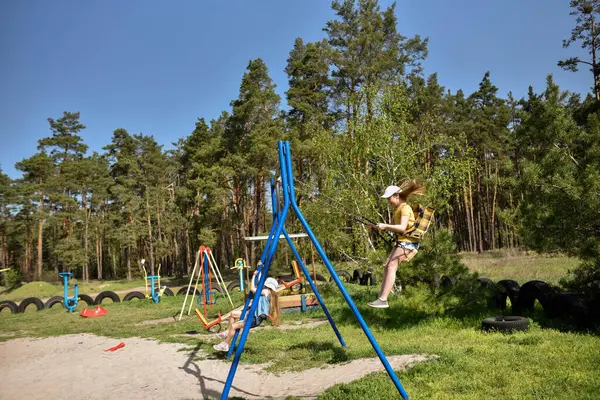 İki sarışın liseli kız salıncakta sallanıyor bir çocuk parkında çam ormanının yakınında