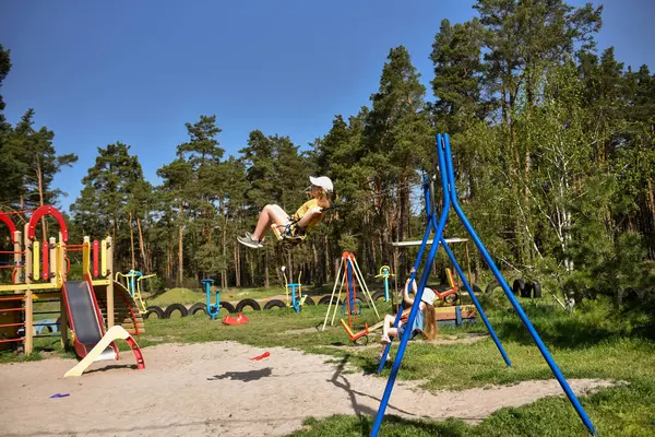 İki sarışın liseli kız salıncakta sallanıyor bir çocuk parkında çam ormanının yakınında
