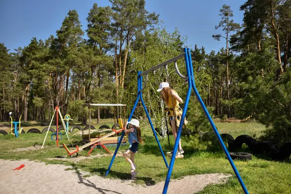 İki sarışın liseli kız salıncakta sallanıyor bir çocuk parkında çam ormanının yakınında