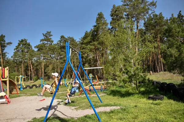İki sarışın liseli kız salıncakta sallanıyor bir çocuk parkında çam ormanının yakınında