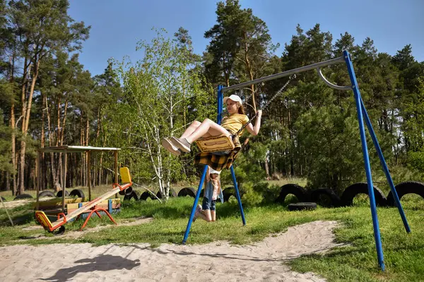 İki sarışın liseli kız salıncakta sallanıyor bir çocuk parkında çam ormanının yakınında