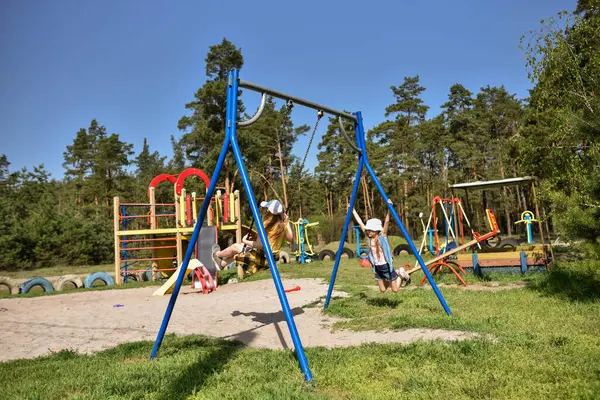 İki sarışın liseli kız salıncakta sallanıyor bir çocuk parkında çam ormanının yakınında