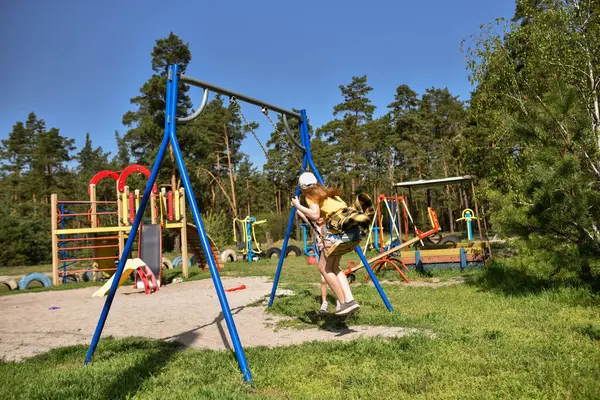 İki sarışın liseli kız salıncakta sallanıyor bir çocuk parkında çam ormanının yakınında