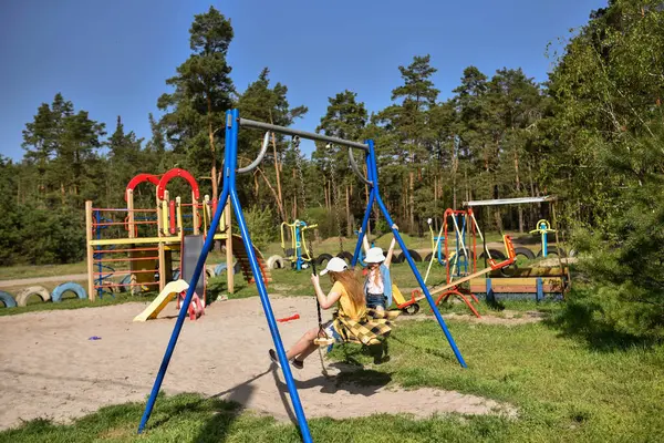 İki sarışın liseli kız salıncakta sallanıyor bir çocuk parkında çam ormanının yakınında