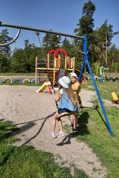 İki sarışın liseli kız salıncakta sallanıyor bir çocuk parkında çam ormanının yakınında