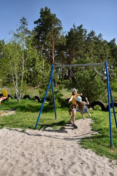 İki sarışın liseli kız salıncakta sallanıyor bir çocuk parkında çam ormanının yakınında