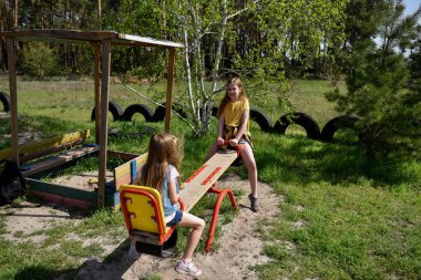 İki neşeli okul çağında kız, şehrin dışındaki bir çam ormanının yakınındaki parkta salıncakta sallanıyor.