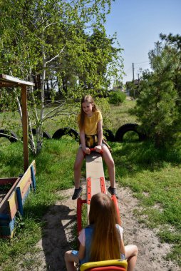 İki neşeli okul çağında kız, şehrin dışındaki bir çam ormanının yakınındaki parkta salıncakta sallanıyor.