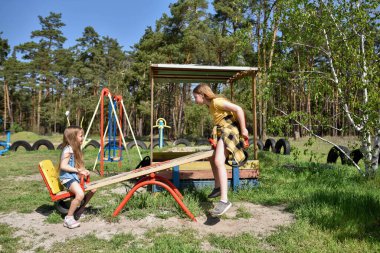 İki neşeli okul çağında kız, şehrin dışındaki bir çam ormanının yakınındaki parkta salıncakta sallanıyor.