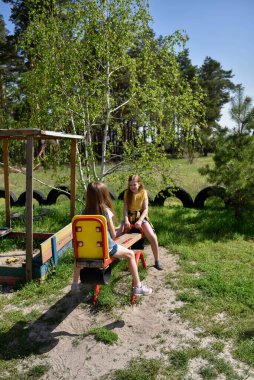 İki neşeli okul çağında kız, şehrin dışındaki bir çam ormanının yakınındaki parkta salıncakta sallanıyor.