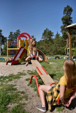 İki neşeli okul çağında kız, şehrin dışındaki bir çam ormanının yakınındaki parkta salıncakta sallanıyor.