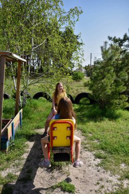 İki neşeli okul çağında kız, şehrin dışındaki bir çam ormanının yakınındaki parkta salıncakta sallanıyor.