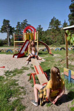 İki neşeli okul çağında kız, şehrin dışındaki bir çam ormanının yakınındaki parkta salıncakta sallanıyor.