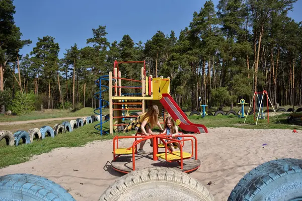 Okul çağındaki çocuklar şehir dışındaki bir çam ormanının yakınındaki bir oyun alanında oynuyorlar. Yaz tatili