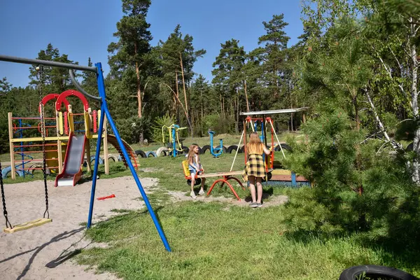 İki neşeli okul çağında kız, şehrin dışındaki bir çam ormanının yakınındaki parkta salıncakta sallanıyor.