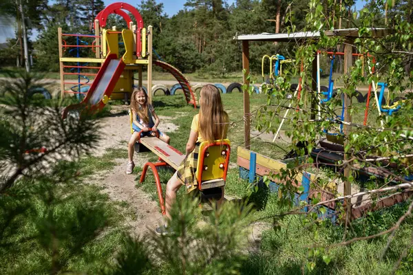 İki neşeli okul çağında kız, şehrin dışındaki bir çam ormanının yakınındaki parkta salıncakta sallanıyor.