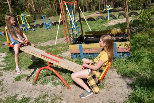 İki neşeli okul çağında kız, şehrin dışındaki bir çam ormanının yakınındaki parkta salıncakta sallanıyor.