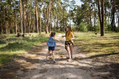 Okul çağındaki tatlı kızlar ormanda bir patikada jimnastik metal bir çemberle oynuyorlar.