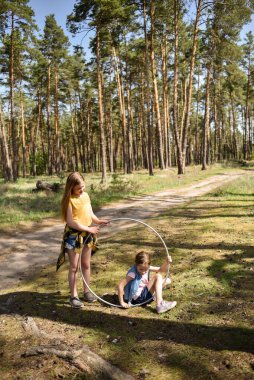 Okul çağındaki tatlı kızlar ormanda bir patikada jimnastik metal bir çemberle oynuyorlar.