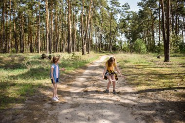 Okul çağındaki tatlı kızlar ormanda bir patikada jimnastik metal bir çemberle oynuyorlar.