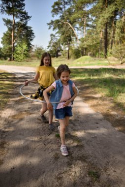 Okul çağındaki tatlı kızlar ormanda bir patikada jimnastik metal bir çemberle oynuyorlar.