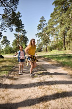 Okul çağındaki tatlı kızlar ormanda bir patikada jimnastik metal bir çemberle oynuyorlar.