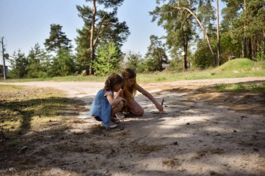 Çam ormanında bir yolda oynayan iki okul çağındaki kız.