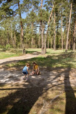 Çam ormanında bir yolda oynayan iki okul çağındaki kız.
