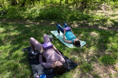 Parktaki minderlerde yoga yapan iki genç kız arkadaş.