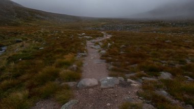 Arkasında bir nehir, bulutlar ve güneş olan bir dağ manzarası.