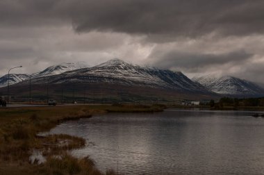 Norveç 'te bulutlu bir gökyüzünün altında, arka planda dağlarla çevrili güzel bir gölün görüntüsü.