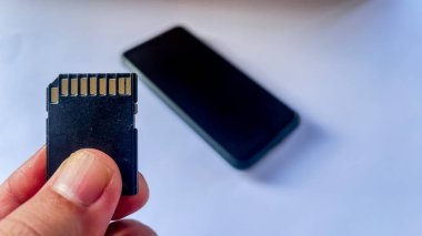 Sol elin sdcard 'ı tutarken beyaz zemin üzerinde akıllı telefon bulanıklığı olan yakın plan görüntüsü. Altın veri okuyucu odak noktası, veri depolama kavramı.