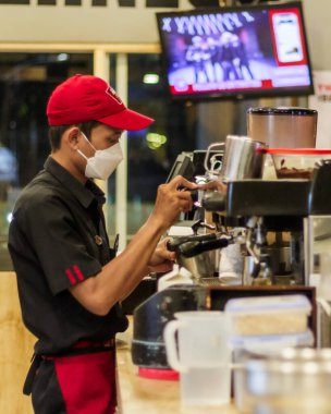 Yogyakarta, Endonezya. 16 Kasım 2022: Kırmızı şapkalı ve beyaz maskeli yakışıklı barista kahve yapıyor.