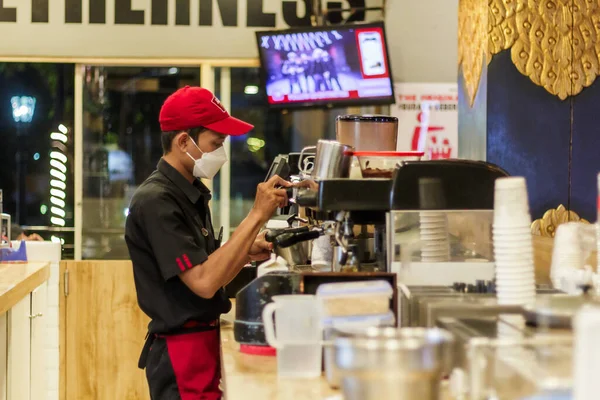Yogyakarta, Endonezya. 16 Kasım 2022: Kırmızı şapkalı ve beyaz maskeli yakışıklı barista kahve yapıyor.