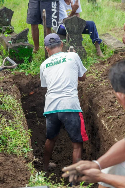 Yogyakarta, Endonezya. 23 Ekim 2022: Beyaz tişörtlü bir adam mezarlıkta mezar kazıyor.