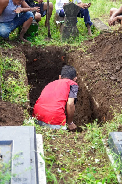 Yogyakarta, Endonezya. 23 Ekim 2022: Kırmızı tişörtlü bir adam mezarlıkta mezar kazıyor.