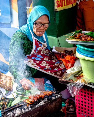 Yogyakarta, Endonezya - 30 Kasım 2022: Yogyakarta 'nın sonraki Bringharjo Market, Yogyakarta Özel Bölgesi' nde geleneksel bir Yogyakarta sokak yemeği olan satay satan yaşlı bir kadın