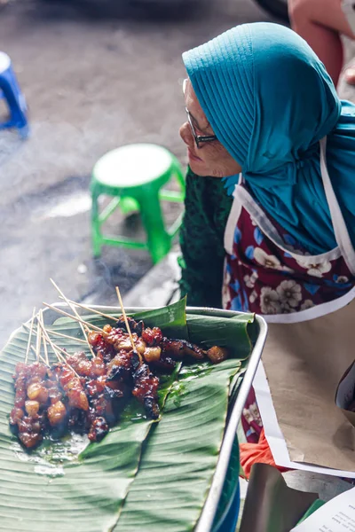 Yogyakarta, Endonezya - 30 Kasım 2022: Yogyakarta 'nın sonraki Bringharjo Market, Yogyakarta Özel Bölgesi' nde geleneksel bir Yogyakarta sokak yemeği olan satay satan yaşlı bir kadın