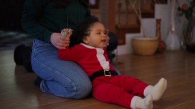Tanımlanamayan beyaz bir kadın Noel Baba kostümlü tatlı Afrikalı Amerikalı bir çocukla oynuyor. Teyzem Noel tatilinin tadını çıkarıyor. Yeğenim evde, oturma odasında.