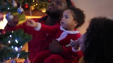 Neşeli baba oğluyla oynuyor. Oturma odasında Noel ağacı süslüyor. Kadınlarla konuşuyor. Olumlu neşe saçan Afro-Amerikan ailesi içeride yeni yıl arifesini kutluyor.