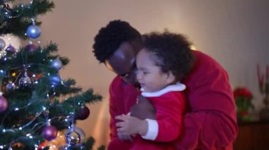 Oyuncu Afrikalı Amerikalı baba ve küçük oğlu Noel arifesinde evde eğleniyorlar. Yeni yıl oyuncaklarıyla oynayan kaygısız bir adam ve çocuğun yan görünüm portresi oturma odasında