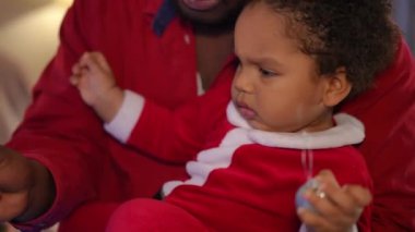 Odaklanmış küçük çocuk evde Noel ağacı süslemesine yardım ediyor. Yeni yıl arifesinde genç bir babayla birlikte oturma odasında Afrika kökenli Amerikalı bir çocuğun portresi.