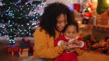 Gülümseyen Afro-Amerikan kadın ve küçük çocuğun portresi Noel arifesinde çengelle oynuyor. Olumlu genç anne ve sevimli meraklı oğul tatilde eğleniyor.