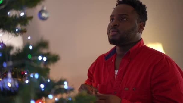 Концентрированный Афроамериканец Украшает Рождественскую Елку Игрушками Канун Нового Года Дома — стоковое видео