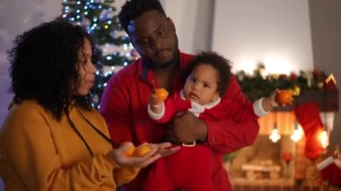 Tatminsiz Afrikalı Amerikalı çocuk, anne ve baba çocuğuyla oynarken ağlıyordu. Noel arifesinde evde Mandarin 'li bir çift ebeveynle tatminsiz küçük bir çocuğun portresi.