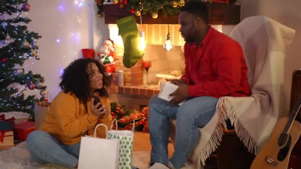 在圣诞节前夕 非洲裔美国女人在网上购物时就像男人在壁炉边看书时的全景肖像 爱说话的年轻夫妇在家里享受新年的乐趣 — 图库视频影像